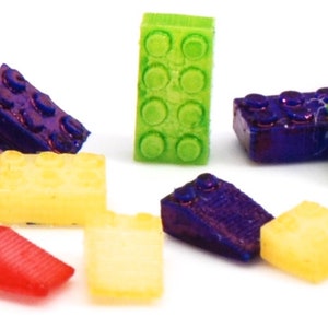 May include: A collection of colorful plastic toy building blocks in various shapes and sizes. The blocks are made of a translucent material and have a glossy finish. The blocks are arranged in a random pattern on a white background.