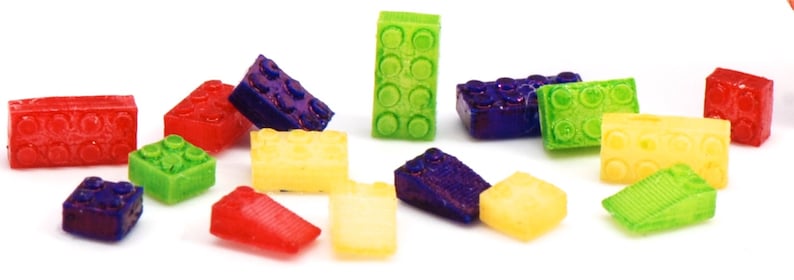 May include: A collection of colorful plastic toy building blocks in various shapes and sizes. The blocks are made of a translucent material and have a glossy finish. The blocks are arranged in a random pattern on a white background.