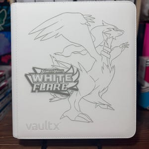 Könnte beinhalten: Weißer Kartenordner mit einer detaillierten Umrisszeichnung einer drachenartigen Kreatur. Das Logo "Scarlet & Violet White Flare" ist sichtbar, zusammen mit dem Markennamen "vaultx". Der Ordner wird auf einem schwarzen Ständer präsentiert.