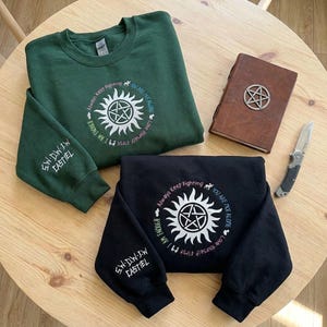 May include: A dark green sweatshirt and a black sweatshirt, each featuring a white circular anti-possession symbol with the text Always Keep Fighting, You Are Not Alone, Love Yourself First, and I Am Enough. The sleeves feature the text S.W.D.W.J.W. CASTIEL.