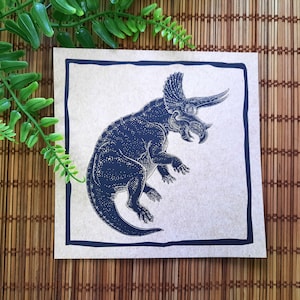 May include: A black and white illustration of a Triceratops dinosaur on a beige background with a black border.