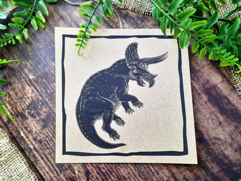 May include: A black and white illustration of a triceratops dinosaur on a brown background. The dinosaur is facing right and has three horns on its head.