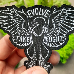 May include: Black embroidered patch with a white outline of a bird with wings spread. The text "EVOLVE" is above the bird and "TAKE FLIGHT" is below the bird.