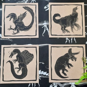 May include: Set of five brown paper cards with black and white illustrations of dinosaurs. The illustrations include a Pterodactyl, a Triceratops, a Stegosaurus, a Tyrannosaurus Rex, and a Velociraptor.