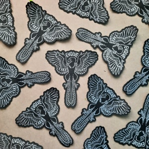 May include: Multiple black iron-on patches with white embroidery. Each patch features a stylised bird with outstretched wings and the text "EVOLVE TAKE FLIGHT".