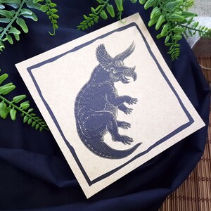 May include: A black and white illustration of a triceratops dinosaur on a brown card with a black border.