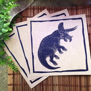 May include: Four brown paper cards with a black border. Each card features a blue illustration of a triceratops dinosaur.