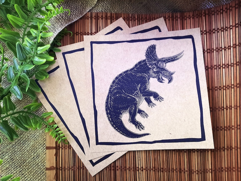 May include: Four brown paper cards with a black border. Each card features a blue illustration of a triceratops dinosaur.