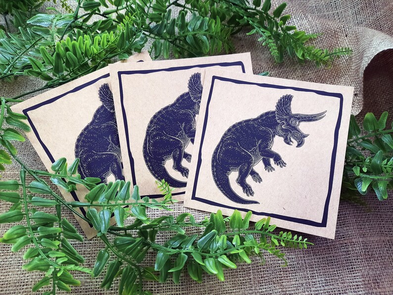 May include: Three brown paper cards with black outlines. Each card features a black silhouette of a triceratops dinosaur.