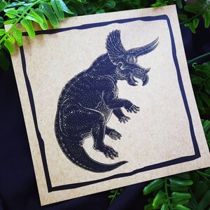 May include: A black and white illustration of a triceratops dinosaur on a brown paper background.
