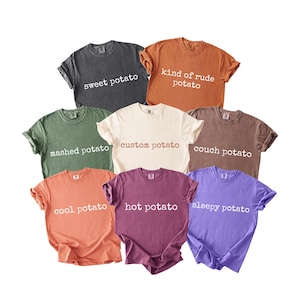 May include: A collection of eight t-shirts in various colors, each with a different potato-themed phrase printed on the front. Colors include gray, orange, green, cream, brown, coral, purple, and lavender. Phrases include "sweet potato" and "kind of rude potato."