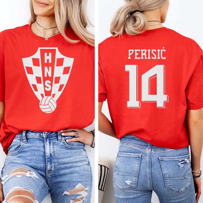 A woman wearing a red t-shirt with a white crest and the number 14 on the back, paired with distressed jeans.