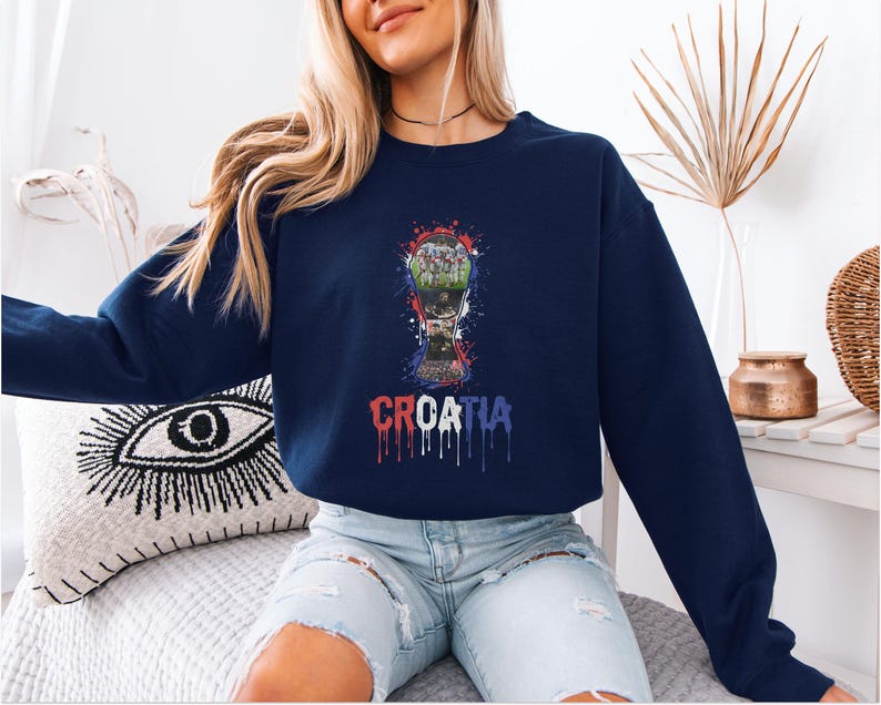 A woman wearing a navy blue sweatshirt with a graphic of a trophy and the word "Crotia" printed on it, sitting on a couch.