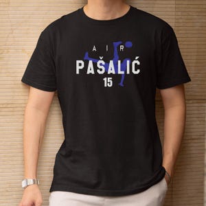 A person wearing a black t-shirt with a graphic design featuring a soccer player and the text "AIR PASALIC 15" printed on it.