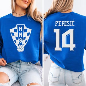 A woman wearing a blue sweatshirt with a white logo and the number 14 on the back.