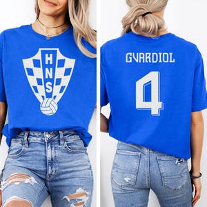 A woman wearing a blue t-shirt with a white shield logo and the name 'GVARDIOL' printed on it, along with the number '4'.