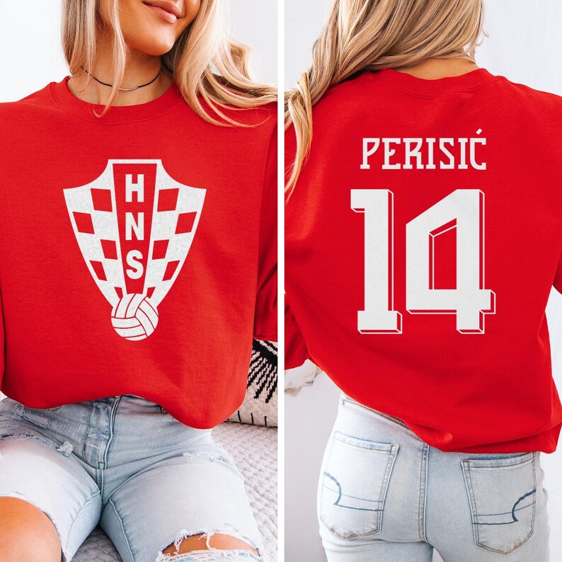 A woman wearing a red shirt with a white crest and the number 14 on the back, sitting on a couch.