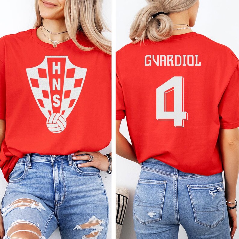 A woman wearing a red t-shirt with a white crest and the number 4 on the back, paired with distressed jeans.