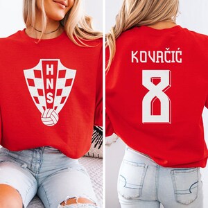A woman wearing a red shirt with a white crest and the number 8 on the back, along with the text "KOVÁCÍK" printed on the back.