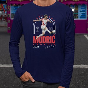 a man in a blue long-sleeved shirt with a graphic design depicting a soccer player in action.