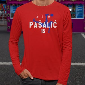 A man wearing a red long-sleeved shirt with the text "AIR PASALIC 15" printed on it.