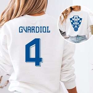 A white sweatshirt with the name 'GVARDIOL' and the number '4' printed on it.