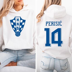 A woman wearing a white hoodie with a blue logo and the number 14 on the back.