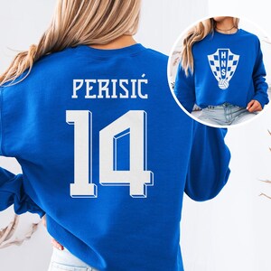A woman wearing a blue sweatshirt with the number 14 and the text "PERISIC" printed on it.