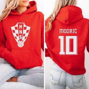 A woman wearing a red hoodie with a white crest and the number 10 on the back.