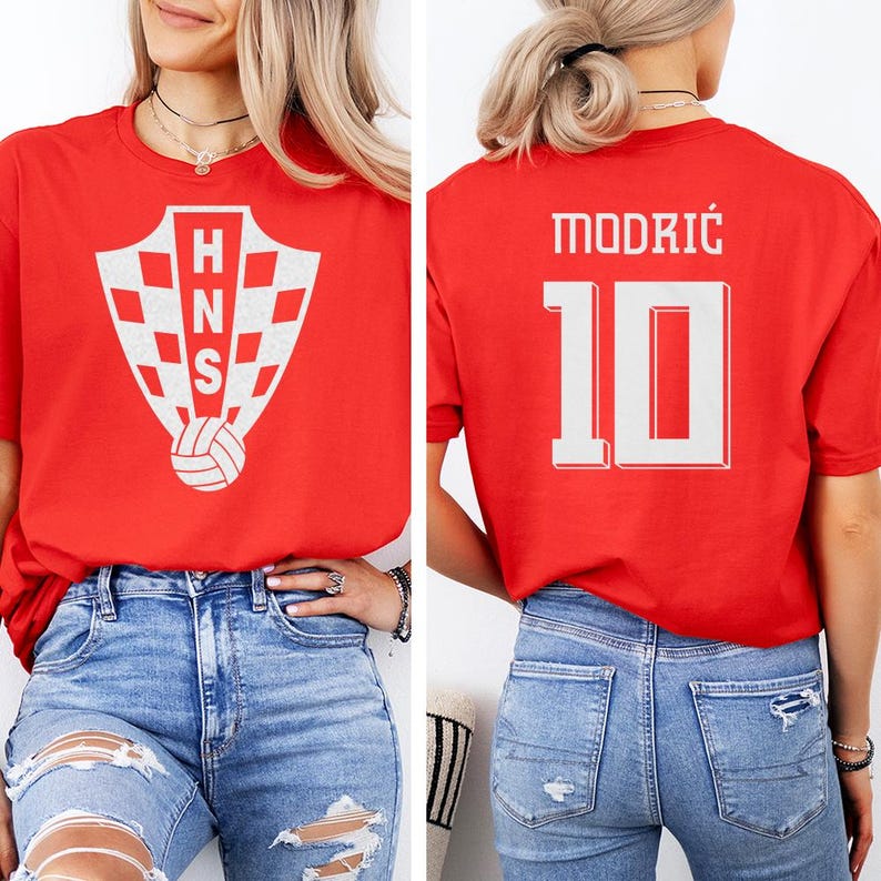 A woman wearing a red t-shirt with a white crest and the number 10 on the back, paired with distressed jeans.