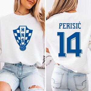 A woman wearing a white sweatshirt with a blue logo and the number 14 on the back.