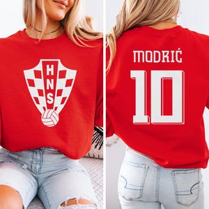 A woman wearing a red shirt with a white crest and the number 10 on it, along with a soccer jersey.