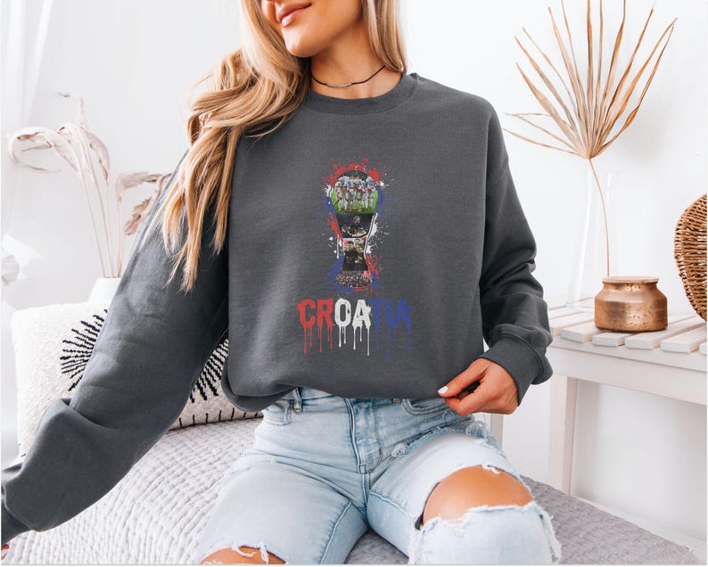 A woman wearing a gray sweatshirt with a graphic design of a soccer ball and the word "CRCATIA" printed on it, sitting on a couch.