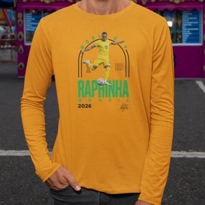 A yellow long-sleeved shirt with a graphic design featuring a soccer player in yellow and the text "RAPRINHA BRAZIL" printed on it.