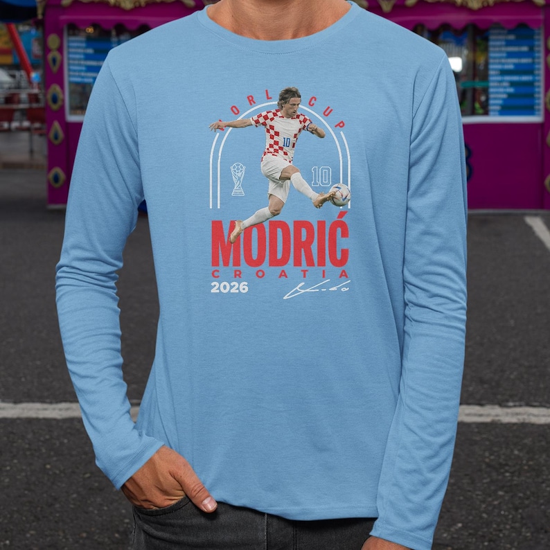 A man wearing a light blue long-sleeved shirt with a graphic design featuring a soccer player and the text "Modric Croatia" printed on it.