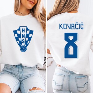 A woman wearing a white sweatshirt with a blue logo and the number 8 on the back.