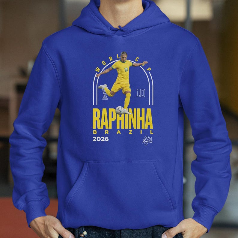 A blue hoodie with a graphic of a soccer player in yellow and white, along with text that reads "RAPHINHA BRAZIL" and "2026".
