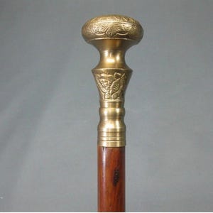 May include: A vintage walking stick with a brass handle and a wooden shaft. The brass handle has an ornate floral design. The shaft is a dark brown colour. The stick is a classic accessory.