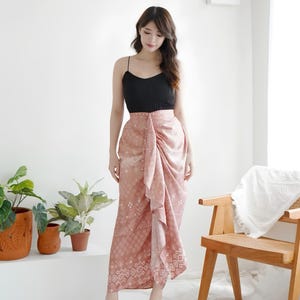 Pode incluir: Uma camisola preta de alças finas combinada com uma saia midi de cintura subida em rosa seco, com um padrão geométrico e floral branco, um painel frontal drapeado e um detalhe franzido lateral que cria uma bainha assimétrica.