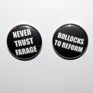 May include: Two circular black pin-back badges with white text. The left badge reads NEVER TRUST FARAGE in all capital letters. The right badge reads BOLLOCKS TO REFORM in all capital letters. Both badges have a smooth, glossy finish.