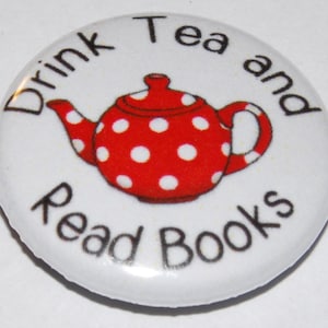 May include: White button with black text that reads "Drink Tea and Read Books". A red teapot with white polka dots is in the centre of the button.