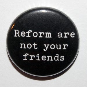 May include: A circular black pin-back badge featuring the white text "Reform are not your friends" printed in a typewriter-style font. The badge has a smooth, glossy finish and a simple, clean design with high contrast between the text and background.