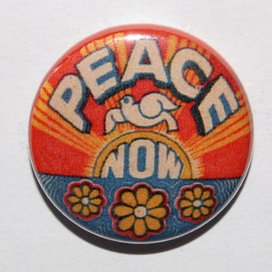 May include: A round button featuring a red, orange and yellow sunburst design. The words "Peace Now" are in white letters with a blue outline. A white dove with a blue outline is perched on top of the word "Now". Three yellow flowers with orange centres are at the bottom of the button.