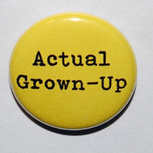 May include: Yellow button with black text that reads "Actual Grown-Up".