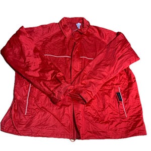 Puede incluir: Una chaqueta roja brillante con cuello y cierre de cremallera. La chaqueta tiene ribetes blancos a lo largo de la cremallera y los bolsillos. Una pequeña etiqueta es visible en la parte inferior derecha. La chaqueta es de un material brillante y ligero.
