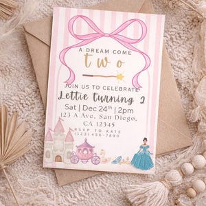 Puede incluir: Una tarjeta de invitación rosa y blanca con el texto "A DREAM COME TWO" y "Lettie turning 2". La tarjeta presenta ilustraciones de un castillo, un carruaje y una princesa. La invitación está en un sobre marrón.