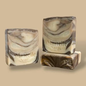May include: Three square soaps with a marbled design in shades of brown and cream. The soaps are stacked and arranged to show the swirling patterns. The text "Martelle Soaps" is embossed on the front of two soaps.