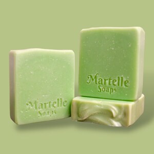 May include: Three square, light green soaps are stacked and arranged on a light green background. The top two soaps have the words "Martelle Soaps" embossed on them. The bottom soap has a swirled design.