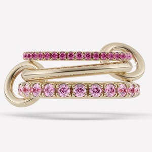 May include: A gold-toned ring set featuring three interconnected bands. Two bands are adorned with pink gemstones, while the central band is plain. The ring set is designed with a unique, linked structure.