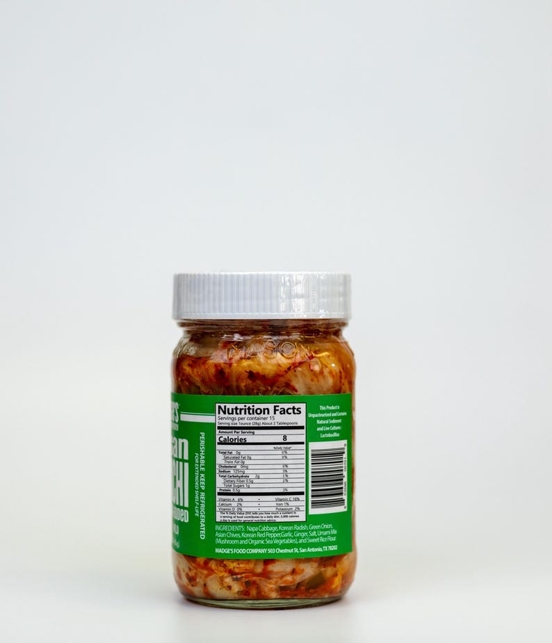May include: A glass jar of kimchi with a white lid and a green label. The label displays nutrition information and ingredients. The kimchi is a mix of red and white vegetables. The jar is labelled "PERISHABLE KEEP REFRIGERATED".